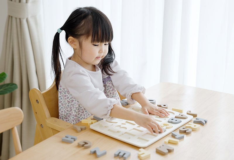 Young girl placing wooden alphabet letters into a puzzle tray while learning through play at home