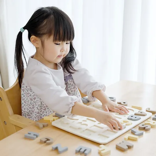 Young girl placing wooden alphabet letters into a puzzle tray while learning through play at home