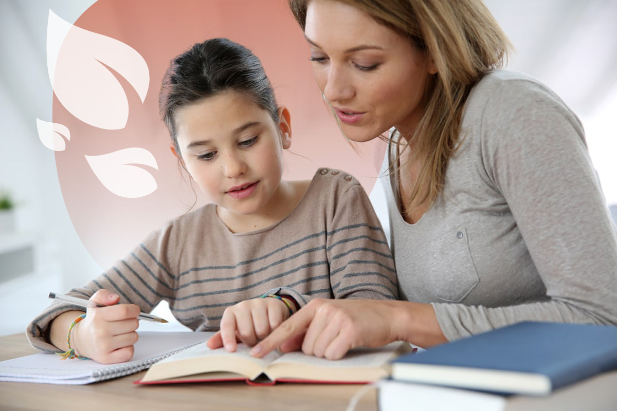 A homeschooling mother and daughter sat at a desk reading through a book. The girl is holding a pen with a notepad. The mother is helping the child homeschool.