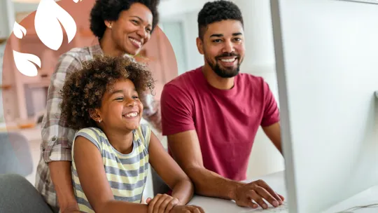 Smiling parents and child at home using a desktop computer for learning