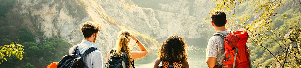Young people on a hike, overlooking a lake surrounded by mountains. 