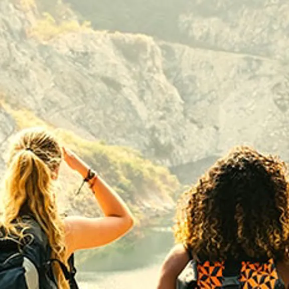 Young people on a hike, overlooking a lake surrounded by mountains.