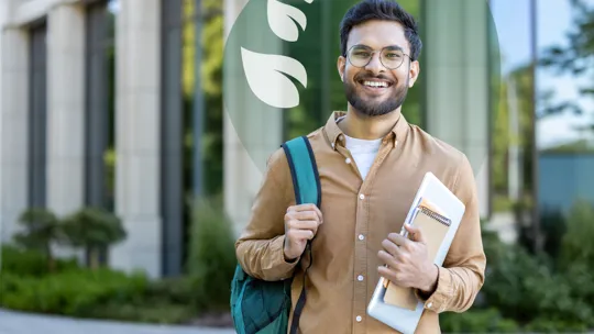A smiling man wearing glasses, a brown shirt, and a backpack, stands outdoors holding a laptop and notebooks. A building and greenery are in the background. A translucent green overlay with white leaves is in the top right.