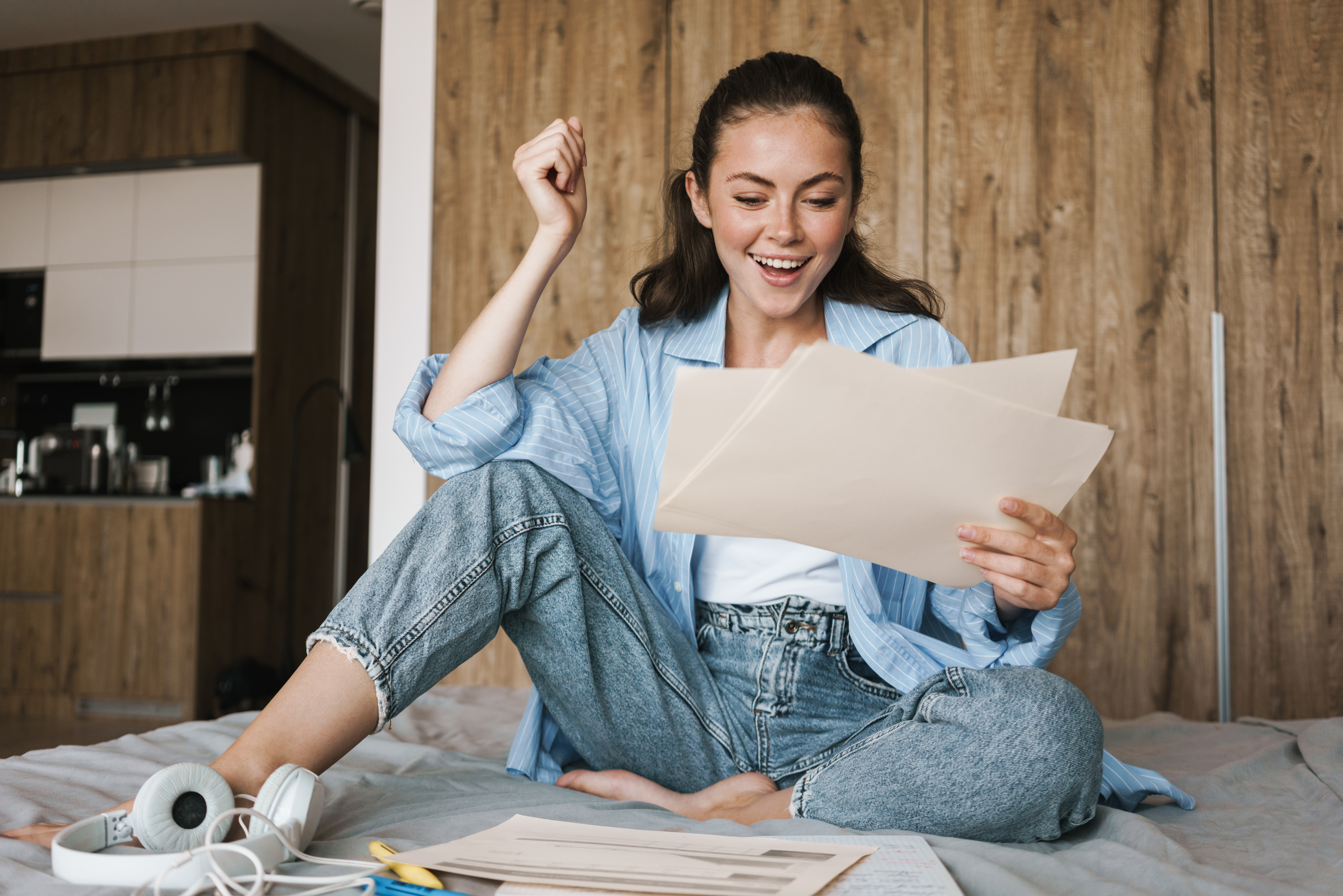 A delighted Wolsey Hall student sits on her bed, excitedly reviewing documents and celebrating her achievement as a Cambridge Learner Award winner.