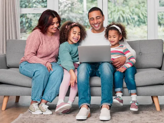 Happy family sitting on sofa, gathered around a laptop for learning or leisure