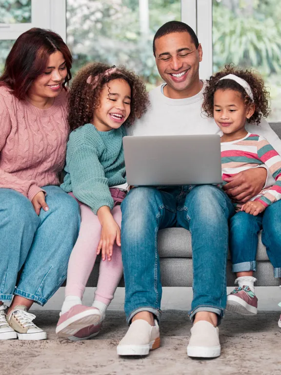 Happy family sitting on sofa, gathered around a laptop for learning or leisure