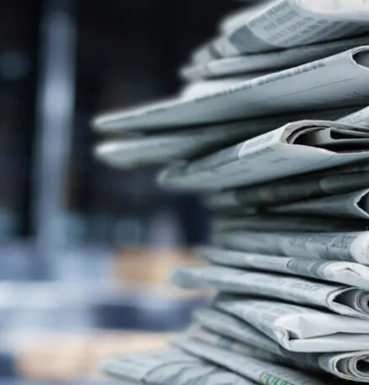 A pile of newspapers stacked on a desk.