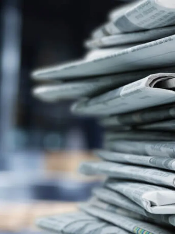 A pile of newspapers stacked on a desk.