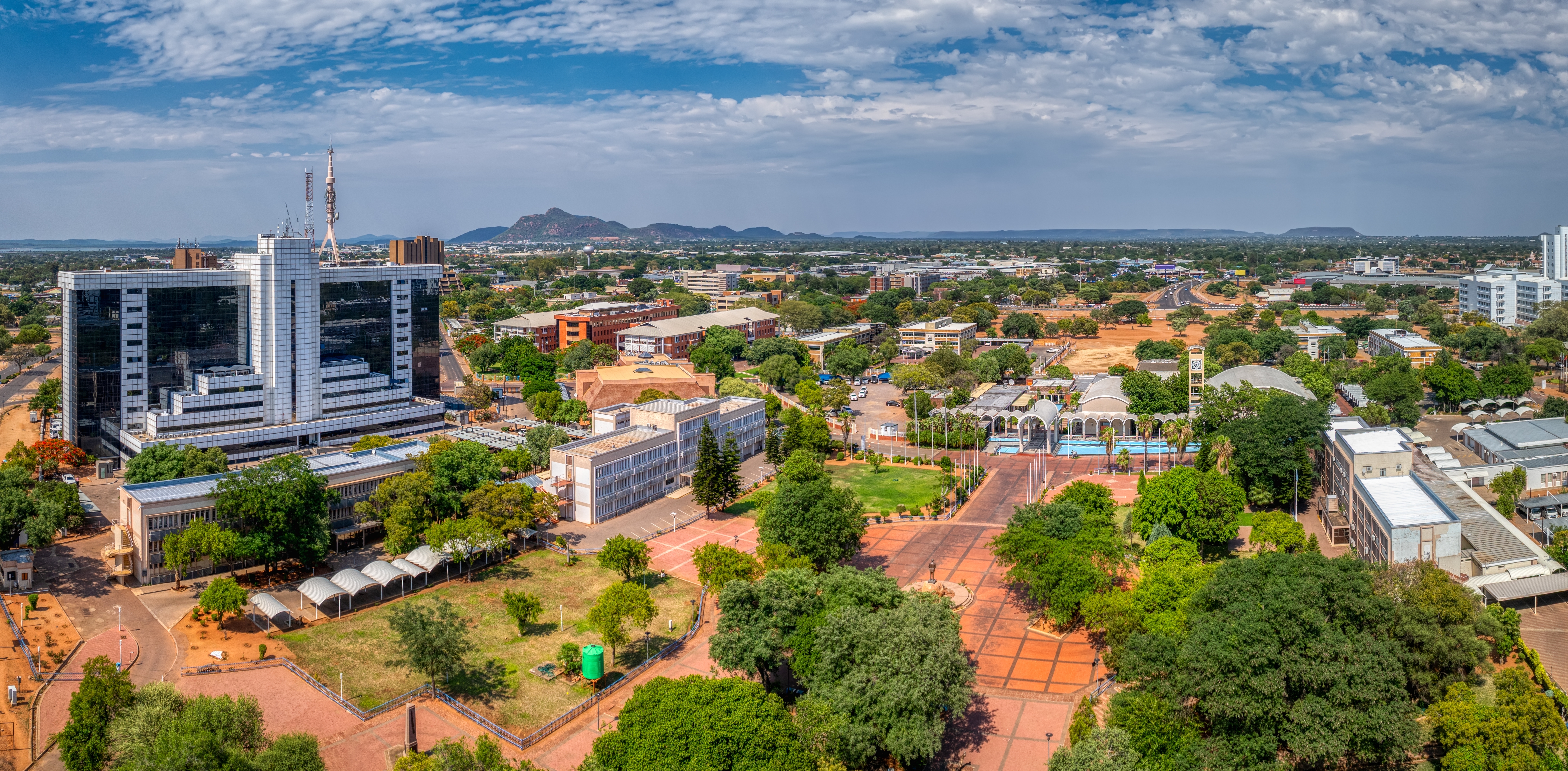 Aerial view of Gaborone, Botswana with government buildings, tree-lined streets and distant hills.
