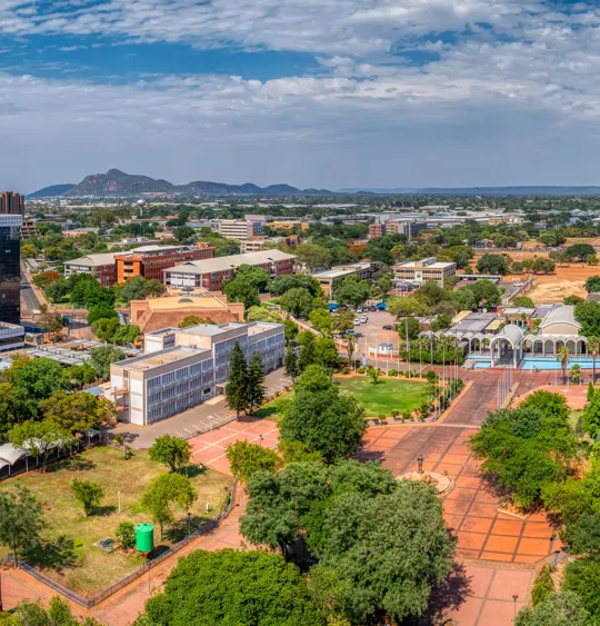 Aerial view of Gaborone, Botswana with government buildings, tree-lined streets and distant hills.