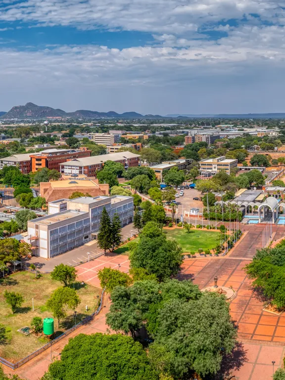 Aerial view of Gaborone, Botswana with government buildings, tree-lined streets and distant hills.