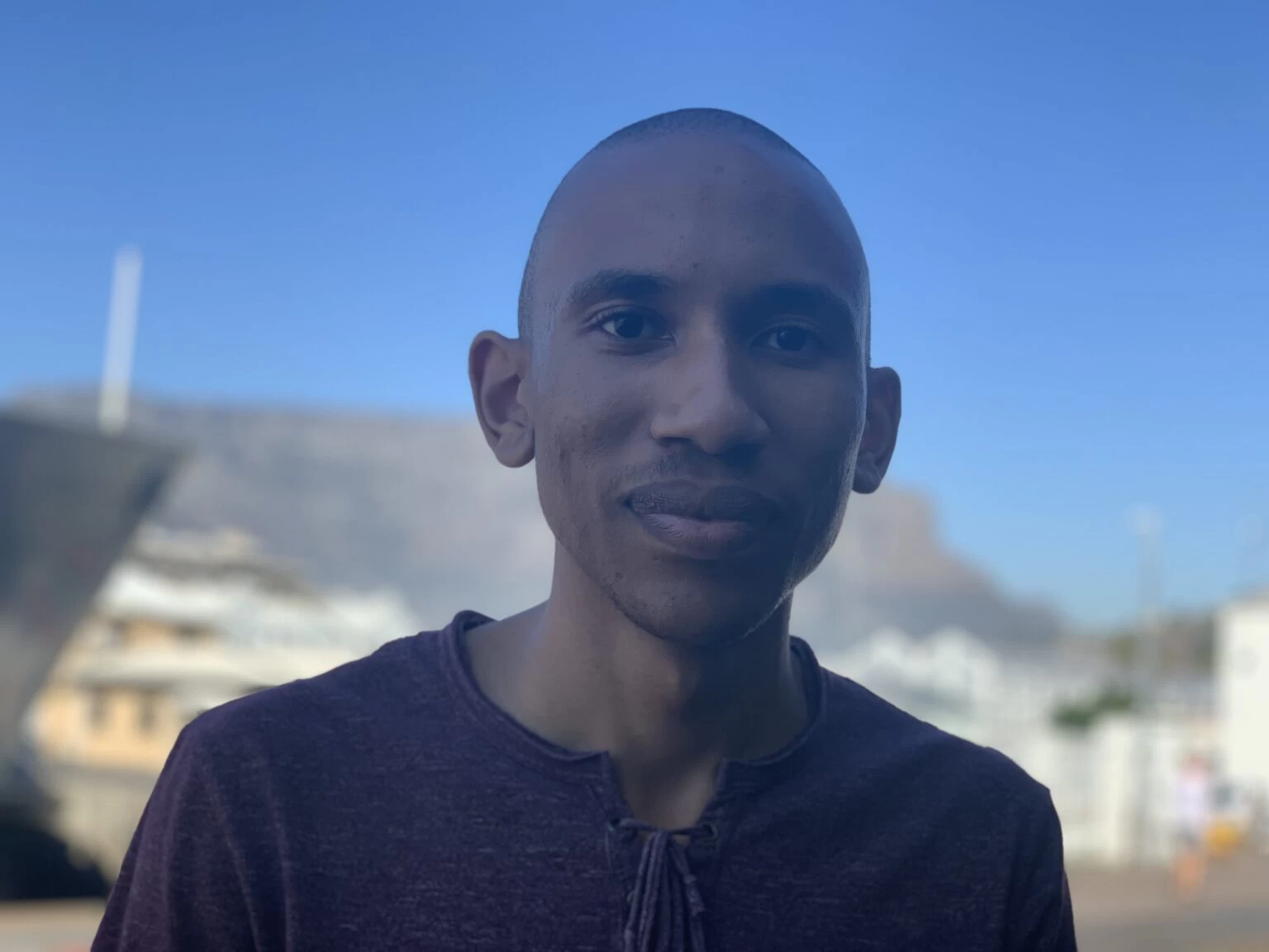 A man smiling, with a blurred background of a city and mountains.