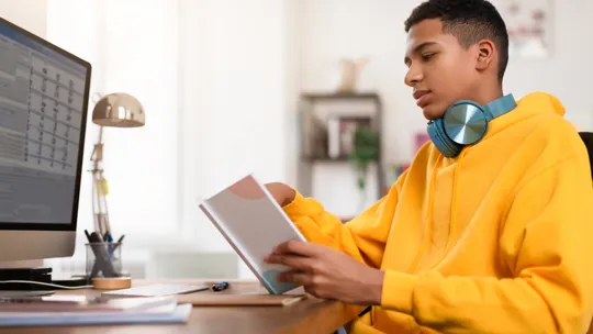 A focused teenage student works at his desk with a schedule on his computer screen, illustrating one of the key benefits of structured homeschooling: a personalised and organised learning environment.