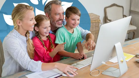 Family gathered around a computer screen, smiling and engaged in online learning