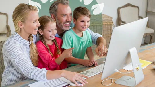 Family gathered around a computer screen, smiling and engaged in online learning