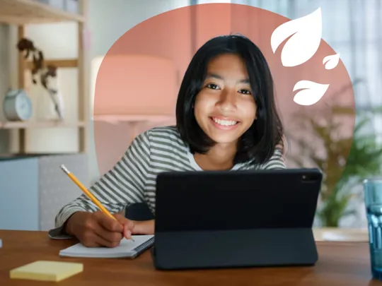 A homeschooling female student with short black hair studying at her bedroom desk, smiling at the camera.