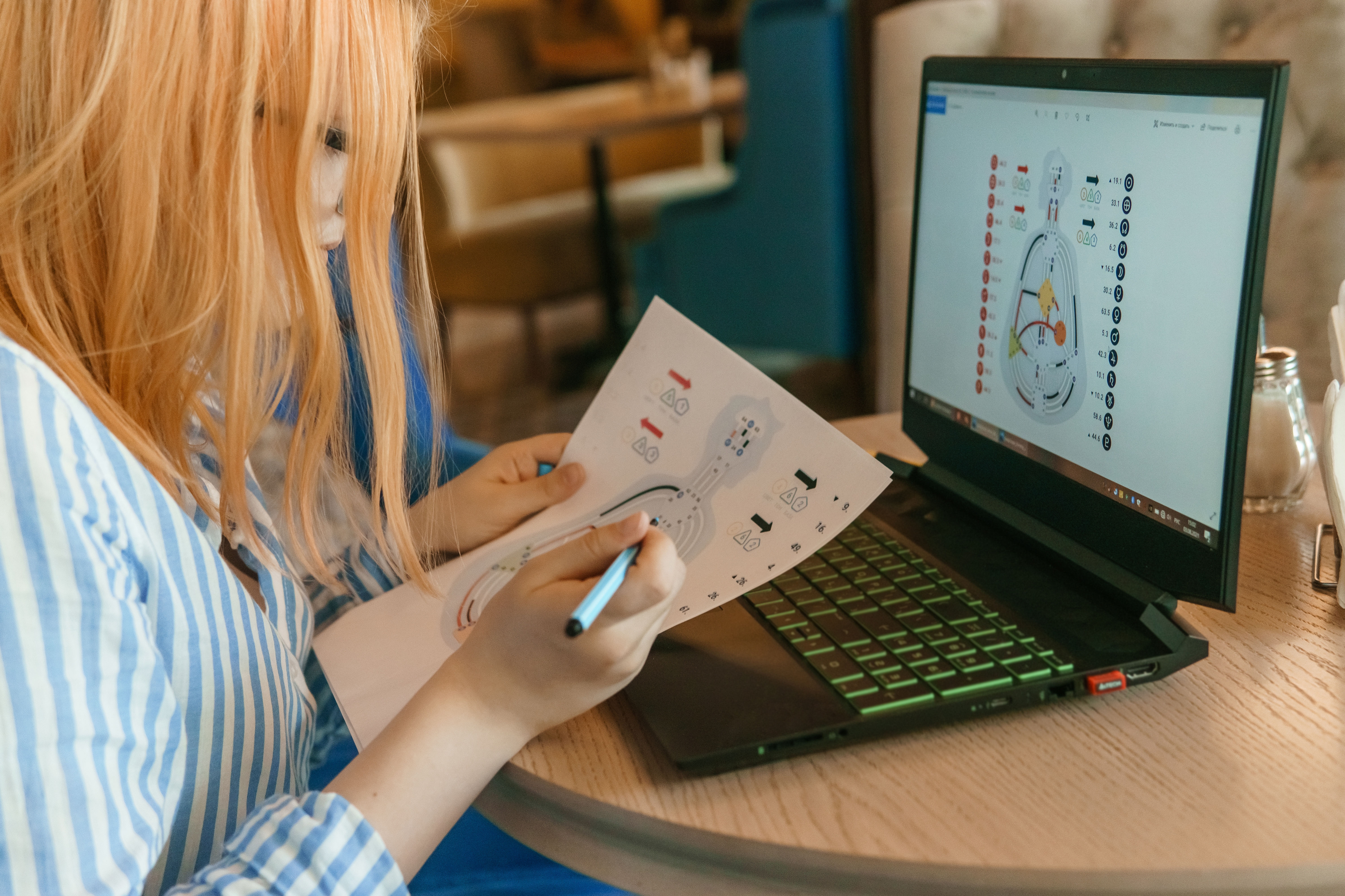 A student with long hair studies a colour-coded diagram while seated at a round table with a laptop open, showing the same visual.