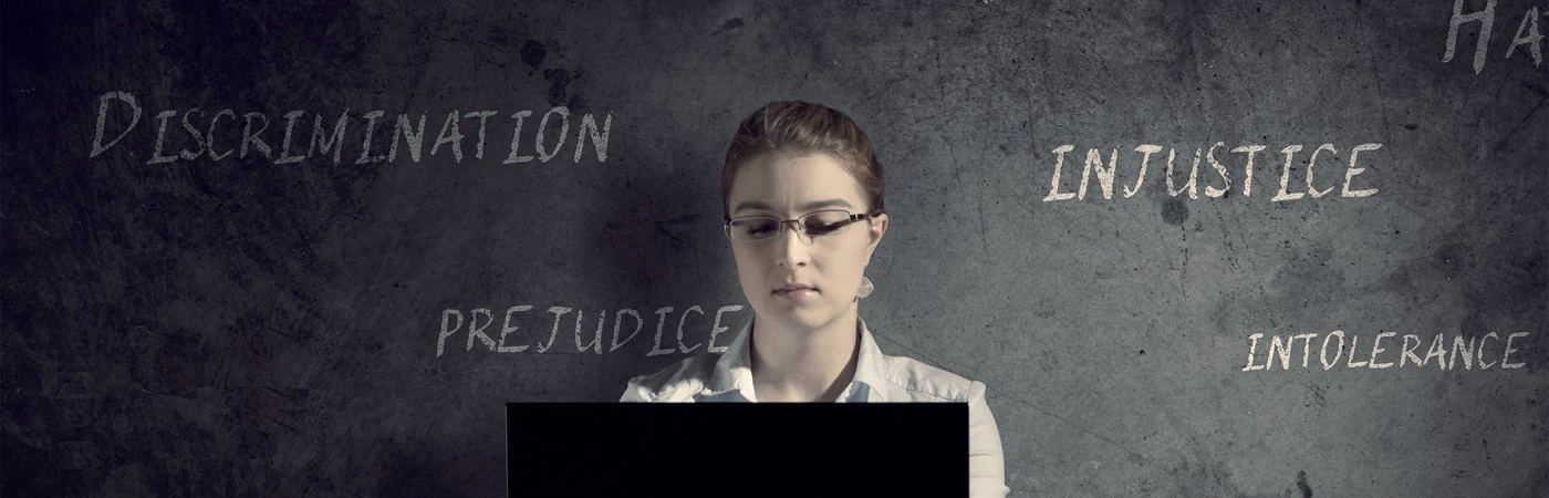 Woman using laptop in front of a dark wall with words like discrimination and prejudice