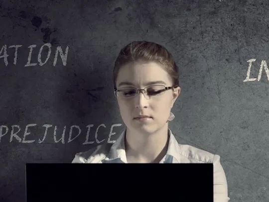 Woman using laptop in front of a dark wall with words like discrimination and prejudice