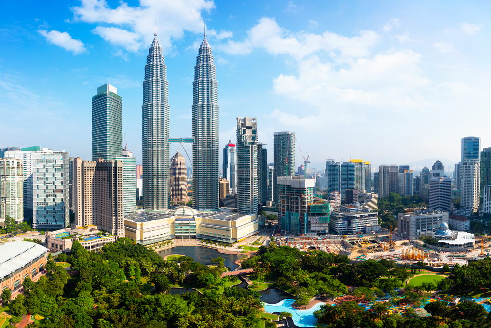 Sunny daytime view of the Kuala Lumpur skyline, featuring the iconic Petronas Towers and surrounding cityscape.