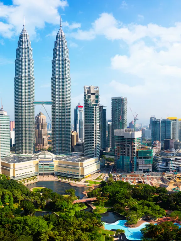 Sunny daytime view of the Kuala Lumpur skyline, featuring the iconic Petronas Towers and surrounding cityscape.