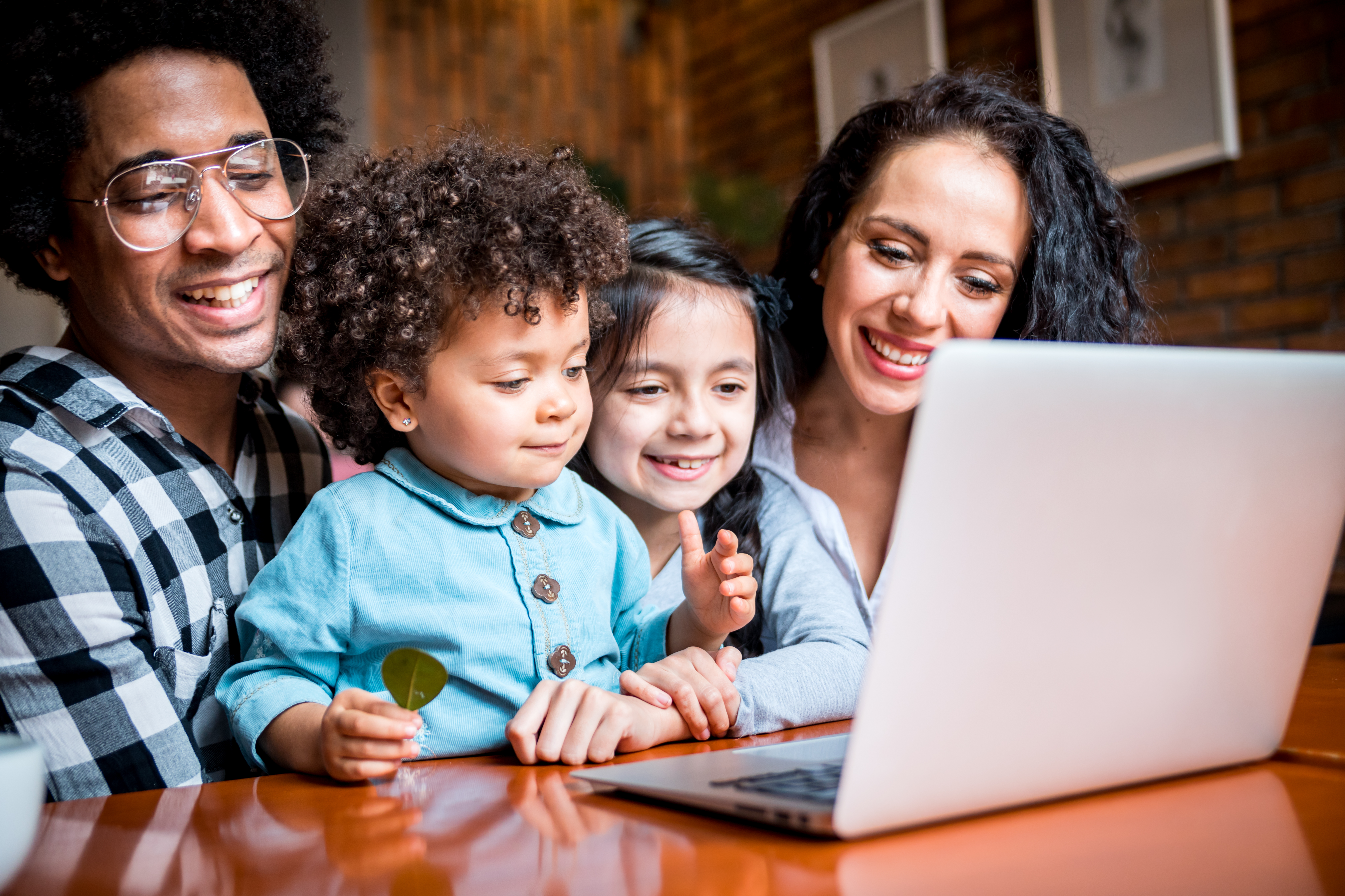 A smiling family with two young children actively participating in an online homeschooling open event on a laptop.