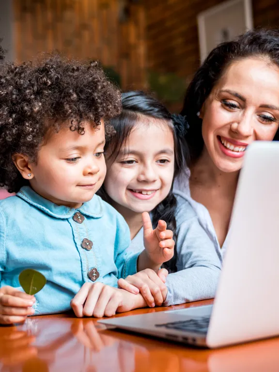 A smiling family with two young children actively participating in an online homeschooling open event on a laptop.