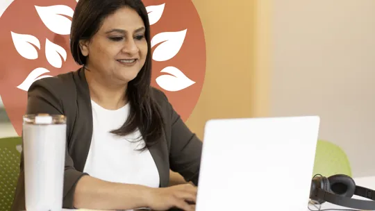 A female tutor sits at a desk, focused on her work while using a laptop computer.