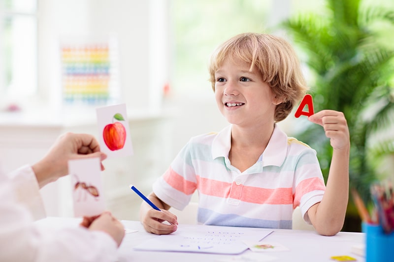 Smiling child holding letter A and matching it with flashcards during a phonics activity at home