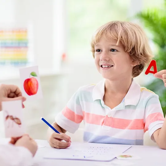 Smiling child holding letter A and matching it with flashcards during a phonics activity at home