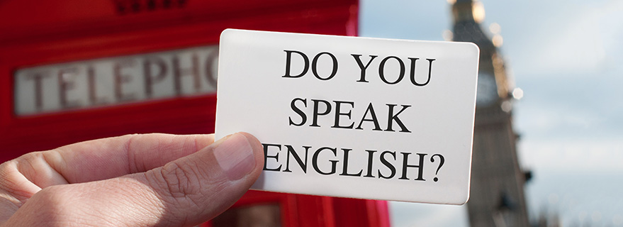 Close-up of a hand holding a card that reads ‘Do you speak English?’ with a red telephone box in the background.
