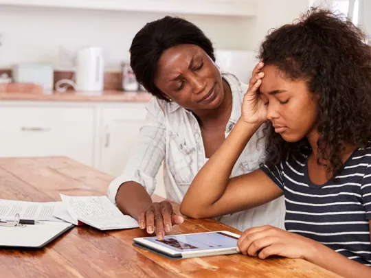 Mother helping teenage daughter with her studies, whilst she faces a moment of distress from anxiety.