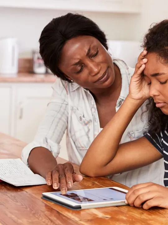 Mother helping teenage daughter with her studies, whilst she faces a moment of distress from anxiety.