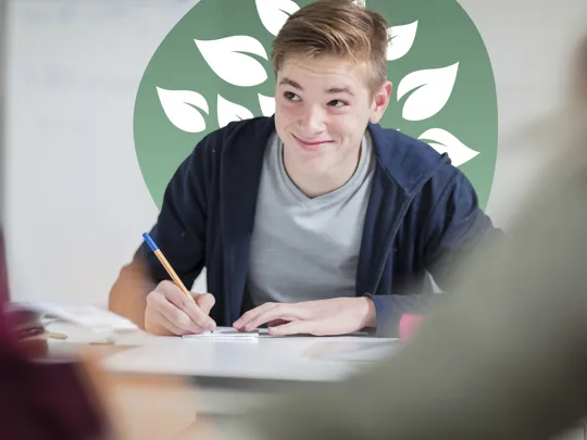 Teenage boy in casual clothing smiling while writing in a notebook during study.