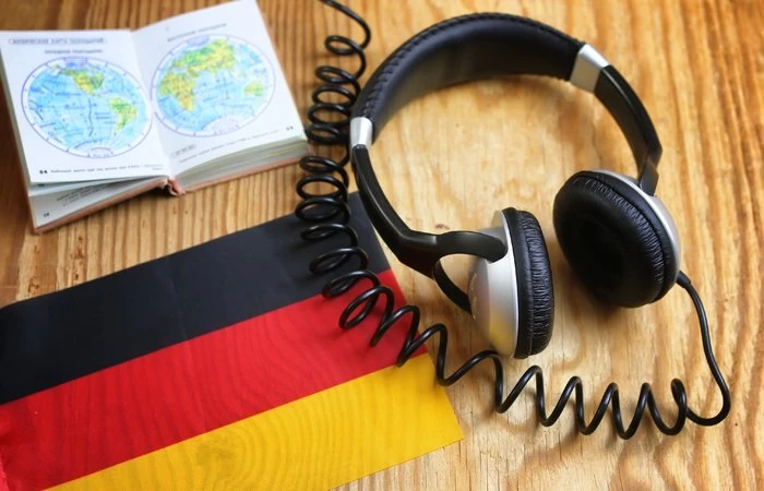 Headphones on a table next to the Germany flag, and a map of the word, showing someone learning the German language. 