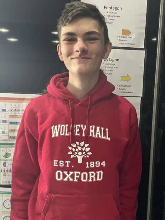 A photograph of a male Wolsey Hall Oxford homeschooling student with short brown hair, wearing a branded jumper and smiling at the camera.