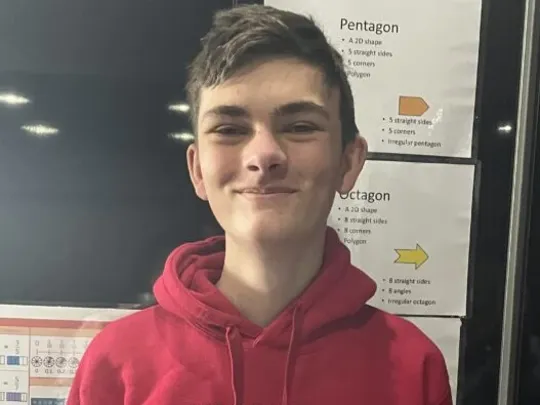 A photograph of a male Wolsey Hall Oxford homeschooling student with short brown hair, wearing a branded jumper and smiling at the camera.