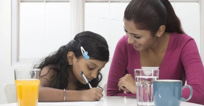A mum homeschooling her young daughter at the kitchen table.