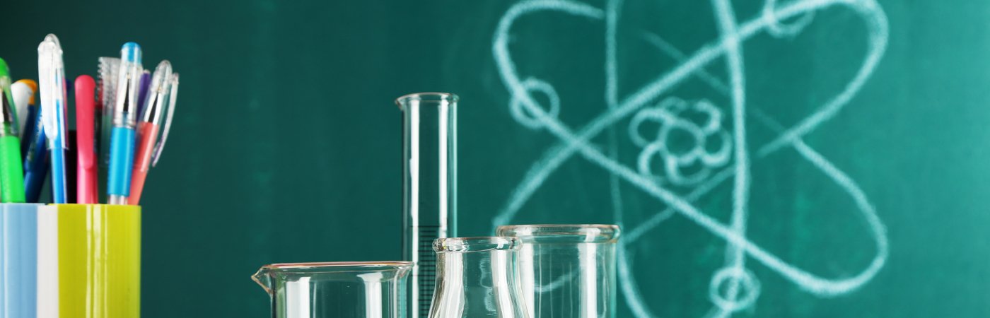 Beakers and test tubes in front of a chalkboard with an atom diagram and colourful pens.