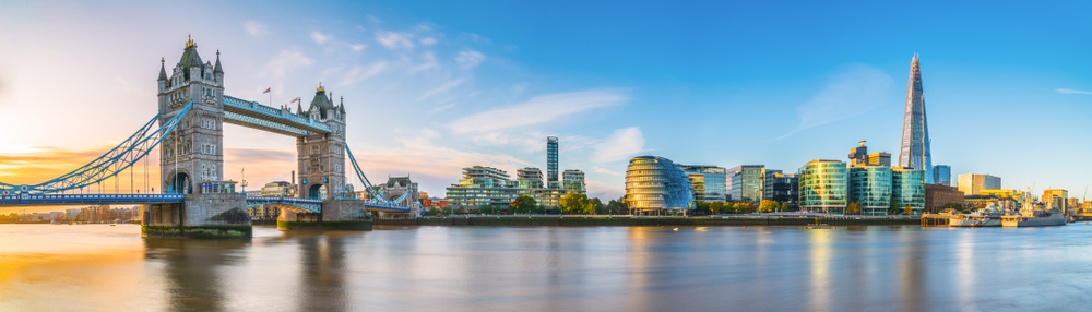 Sunlit view of Tower Bridge and the London skyline, featuring The Shard and city buildings along the Thames.