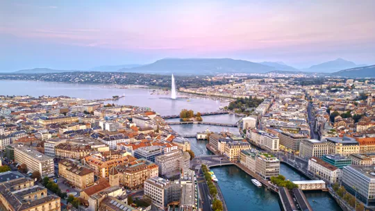 Twilight cityscape of Geneva with Jet d’Eau fountain and mountains in the background