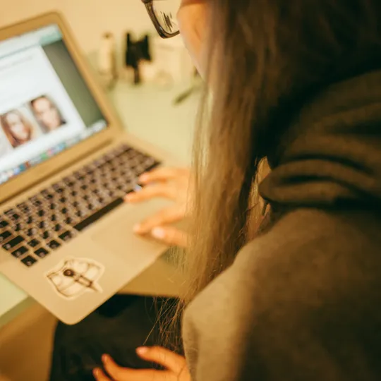 Student using a laptop to view a webpage with images of people, representing safe online interaction and digital safeguarding at Pamoja.
