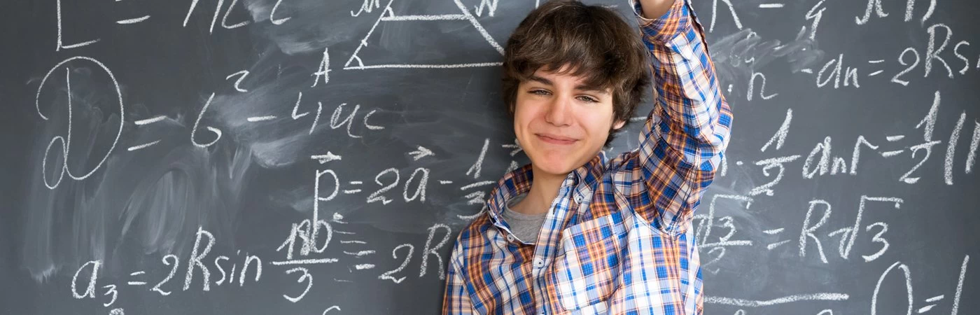 A male student in front of a blackboard with a variety of maths equations on it. 