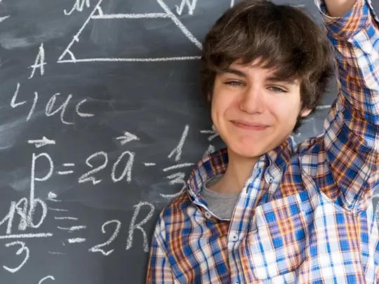 A male student in front of a blackboard with a variety of maths equations on it.