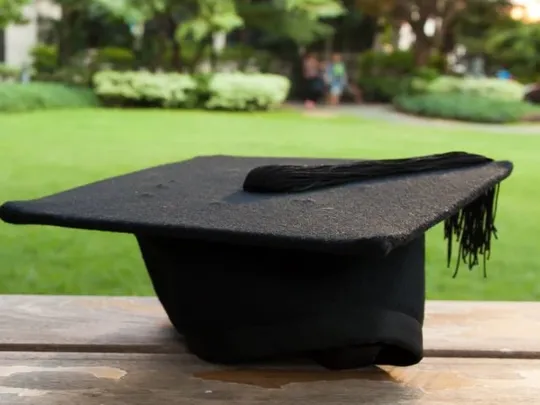 A photograph of a graduation mortarboard on a table next to a field.