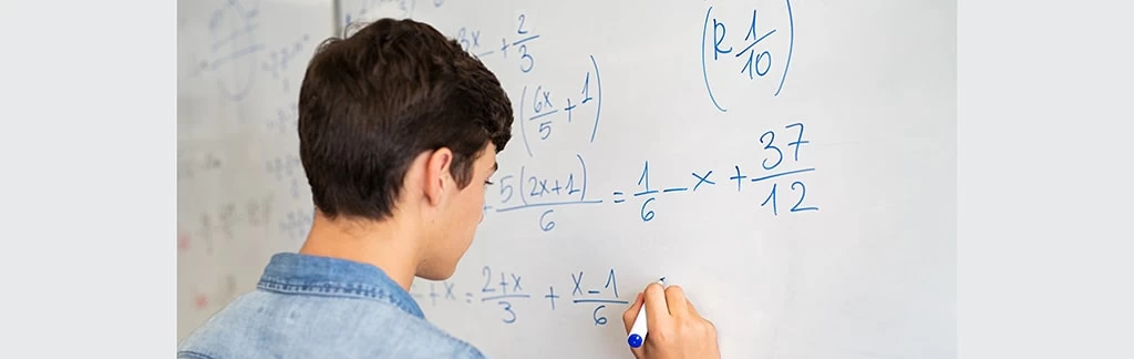 A male student writing maths equations on a whiteboard.