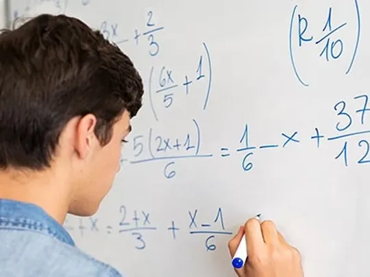 A male student writing maths equations on a whiteboard.