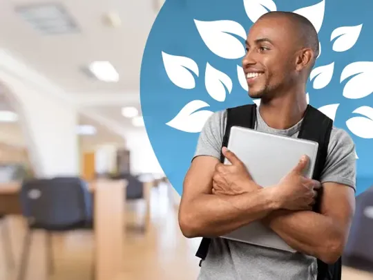 A young man with a black rucksack smiling to the left, holding a laptop to his chest with both arms.
