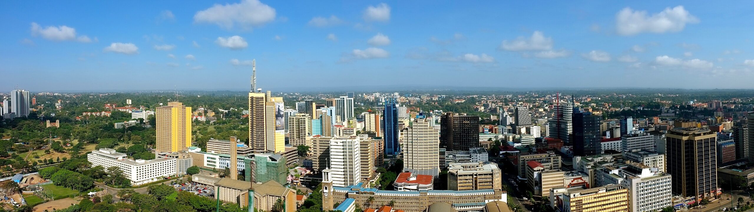 Panoramic view of Nairobi skyline with tall buildings and greenery under a bright blue sky.
