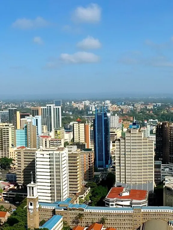 Panoramic view of Nairobi skyline with tall buildings and greenery under a bright blue sky.